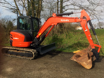 orange coloured Kubota digger U48 outside with trees behind it, bucket facing downwards